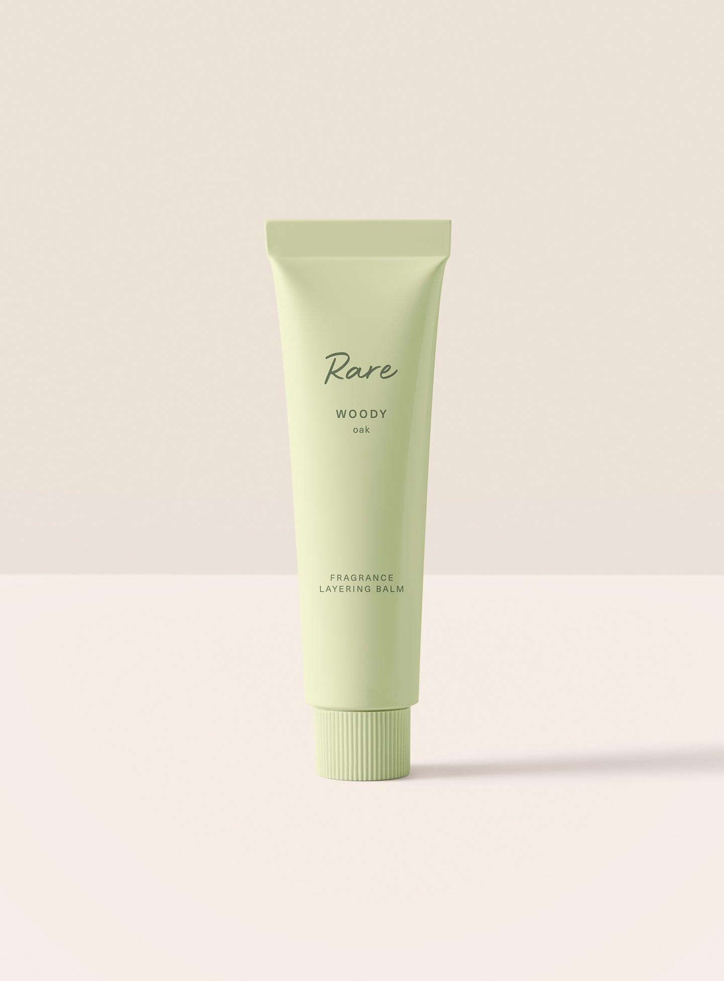 The Rare Woody Oak Fragrance Layering Balm stands upright in its minimalist green packaging.